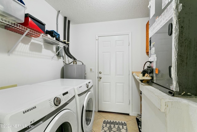 clothes washing area featuring water heater, washer and clothes dryer, light tile patterned flooring, and a textured ceiling