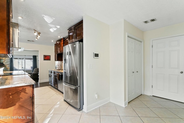 kitchen featuring light stone counters, a textured ceiling, stainless steel appliances, sink, and range hood