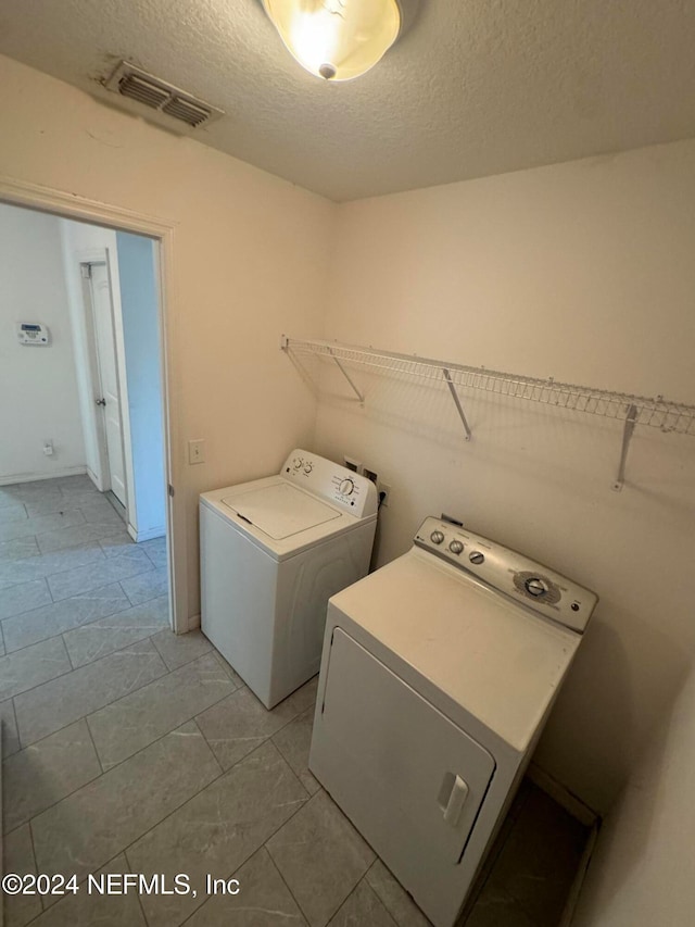 clothes washing area with light tile patterned flooring, a textured ceiling, and washing machine and clothes dryer