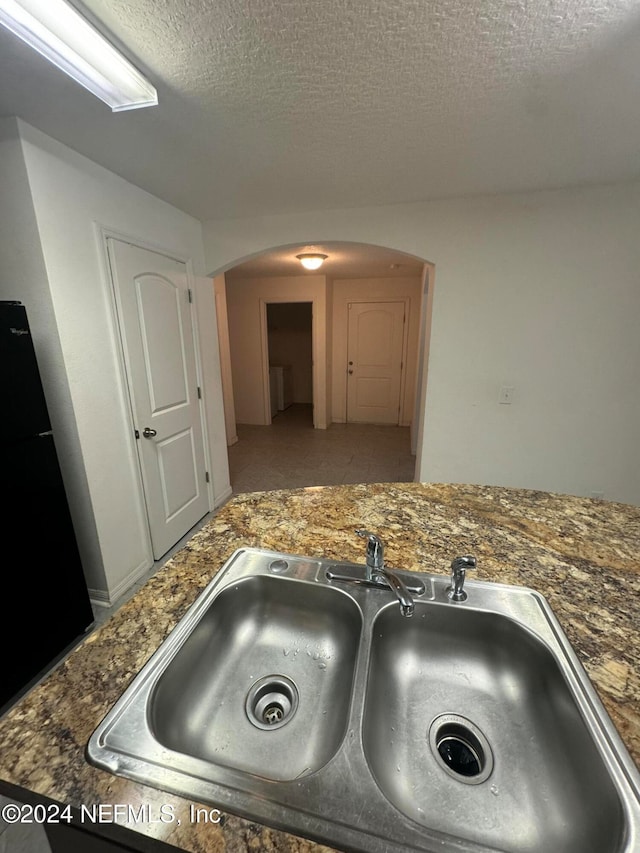 room details featuring black fridge, a textured ceiling, and sink