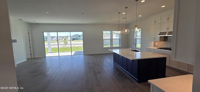 kitchen with under cabinet range hood, open floor plan, a sink, and light countertops