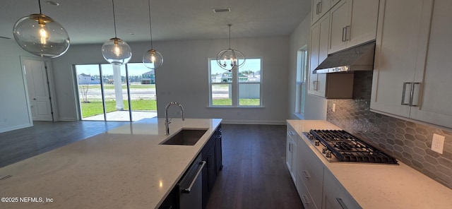 kitchen with a wealth of natural light, a sink, under cabinet range hood, stainless steel gas stovetop, and backsplash