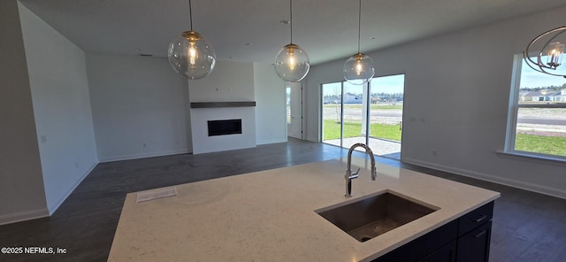 kitchen featuring dark wood-style floors, open floor plan, hanging light fixtures, a fireplace, and a sink