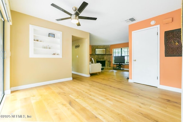 unfurnished living room featuring hardwood / wood-style floors, ceiling fan, a stone fireplace, and built in features