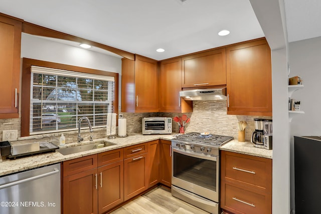 kitchen with light stone countertops, backsplash, stainless steel appliances, sink, and light hardwood / wood-style floors