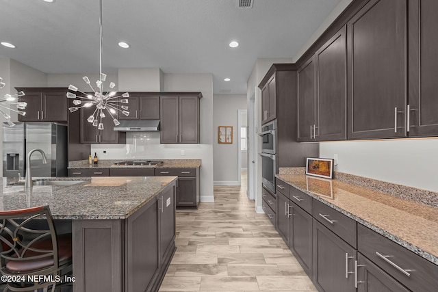 kitchen with stone counters, hanging light fixtures, stainless steel appliances, an inviting chandelier, and a kitchen bar