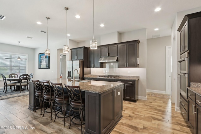 kitchen with under cabinet range hood, appliances with stainless steel finishes, light wood-style flooring, a kitchen breakfast bar, and a sink
