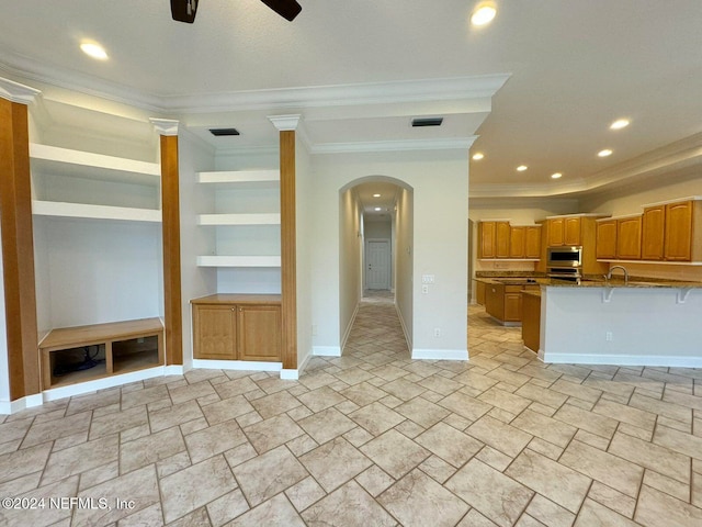 interior space featuring a breakfast bar area, ceiling fan, appliances with stainless steel finishes, and ornamental molding