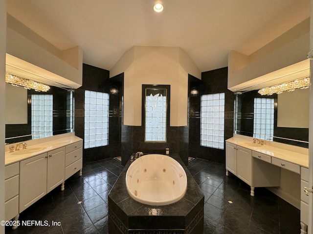 bathroom with tiled tub, tile walls, vanity, vaulted ceiling, and tile patterned floors