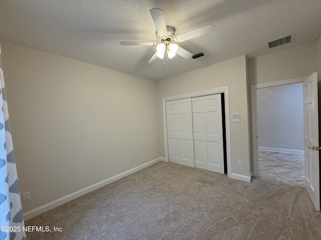 unfurnished bedroom featuring light carpet, ceiling fan, a closet, and a textured ceiling