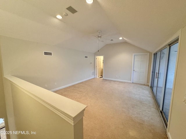 empty room with a textured ceiling, vaulted ceiling, light colored carpet, and ceiling fan