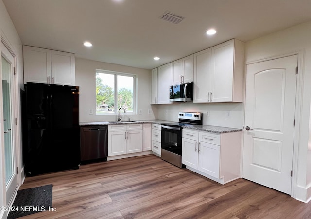 kitchen with light hardwood / wood-style floors, black appliances, sink, light stone countertops, and white cabinetry