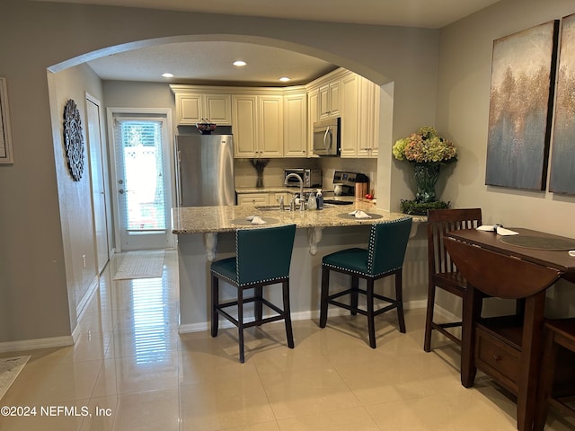 kitchen with a kitchen bar, light stone counters, sink, light tile patterned flooring, and appliances with stainless steel finishes