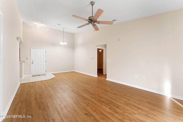 unfurnished room featuring light hardwood / wood-style floors, ceiling fan with notable chandelier, and a towering ceiling