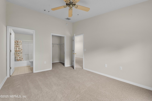 unfurnished bedroom featuring light colored carpet, a spacious closet, baseboards, ensuite bath, and a closet