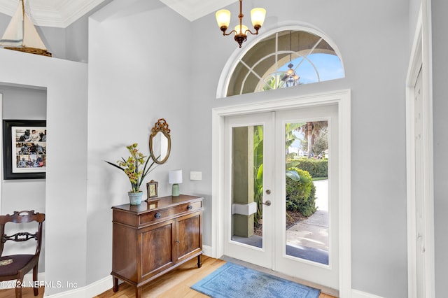 entryway featuring a towering ceiling, light wood-type flooring, crown molding, and a notable chandelier