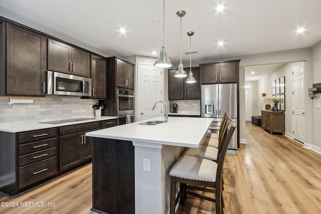 kitchen with appliances with stainless steel finishes, hanging light fixtures, a center island with sink, and light hardwood / wood-style flooring