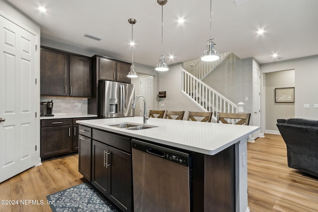 kitchen featuring appliances with stainless steel finishes, pendant lighting, sink, an island with sink, and light hardwood / wood-style floors