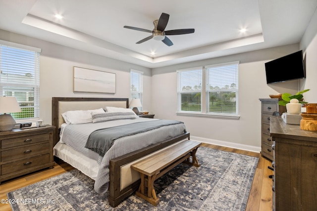 bedroom featuring hardwood / wood-style floors, multiple windows, and a tray ceiling