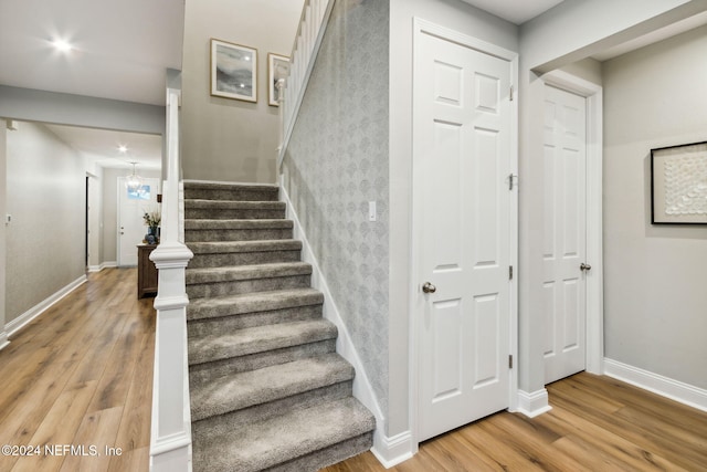 stairs with wood-type flooring and a notable chandelier