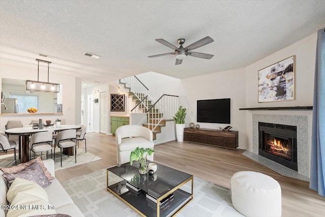 living room featuring a tile fireplace, ceiling fan, light hardwood / wood-style floors, and a textured ceiling