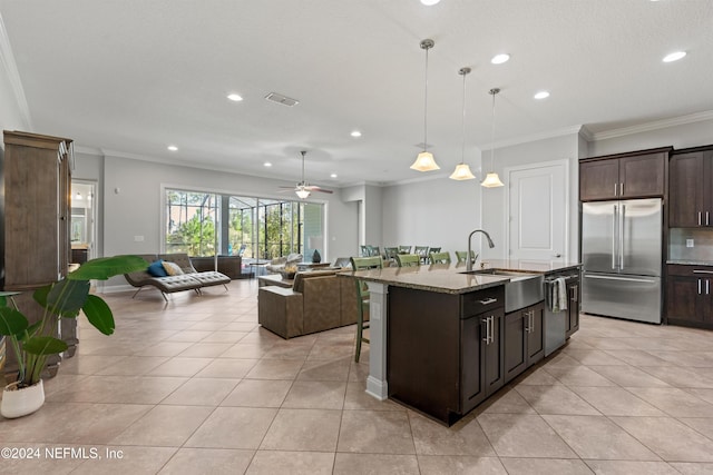 kitchen with ceiling fan, sink, light stone counters, a center island with sink, and appliances with stainless steel finishes