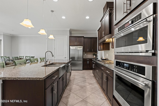 kitchen featuring hanging light fixtures, ornamental molding, an island with sink, appliances with stainless steel finishes, and dark brown cabinetry