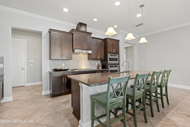 kitchen featuring hanging light fixtures, appliances with stainless steel finishes, dark brown cabinetry, and a kitchen island with sink