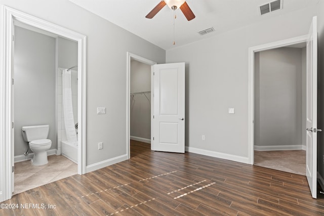 unfurnished bedroom with ensuite bath, ceiling fan, dark wood-type flooring, a spacious closet, and a closet