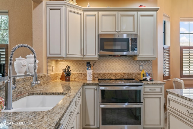 kitchen featuring sink, light stone counters, appliances with stainless steel finishes, and tasteful backsplash