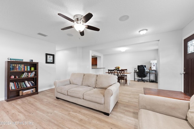 living room featuring ceiling fan, light hardwood / wood-style floors, and a textured ceiling