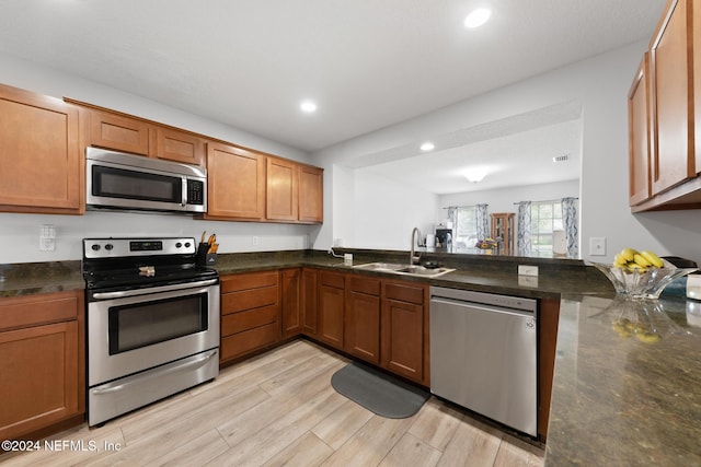 kitchen with appliances with stainless steel finishes, sink, dark stone counters, light hardwood / wood-style floors, and kitchen peninsula