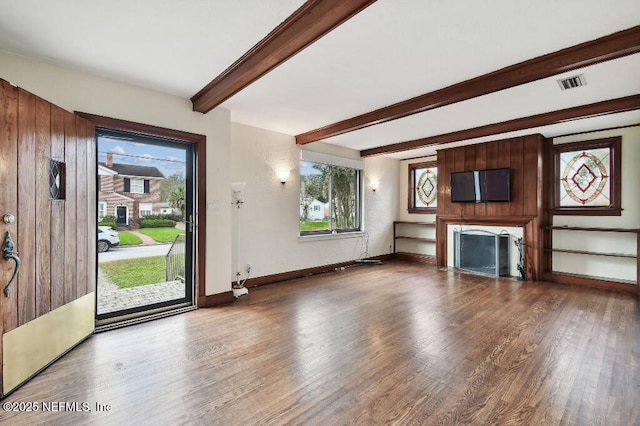 unfurnished living room with a fireplace, wood finished floors, visible vents, baseboards, and beamed ceiling