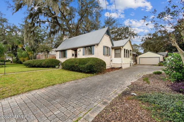 view of front of house featuring brick siding, an outdoor structure, a detached garage, a chimney, and a front yard