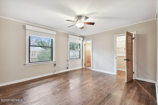 unfurnished bedroom featuring a walk in closet, ornamental molding, a ceiling fan, wood finished floors, and baseboards