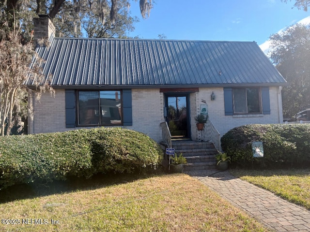 view of front of property featuring a front yard, brick siding, and metal roof