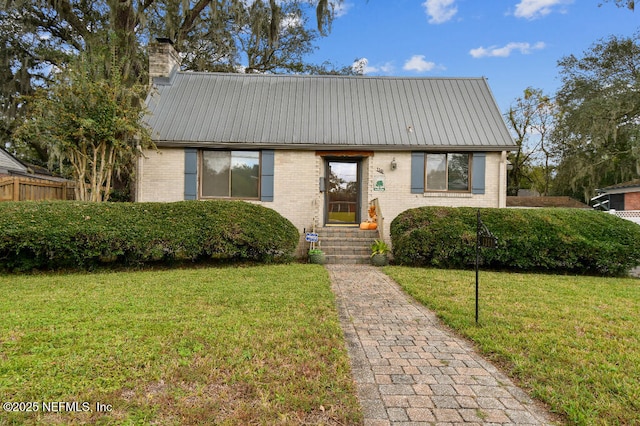 view of front of home with a front yard, a chimney, brick siding, and metal roof