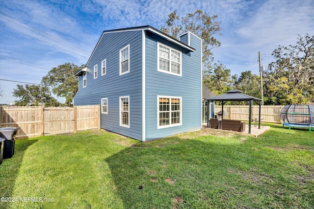 back of property featuring a lawn, a trampoline, a gazebo, and a patio area