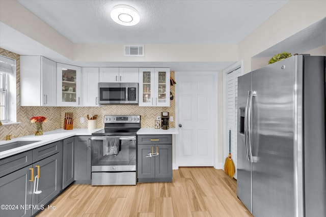 kitchen featuring white cabinetry, appliances with stainless steel finishes, gray cabinetry, light wood-type flooring, and decorative backsplash