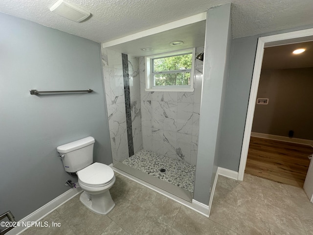 bathroom with tile patterned flooring, tiled shower, a textured ceiling, and toilet