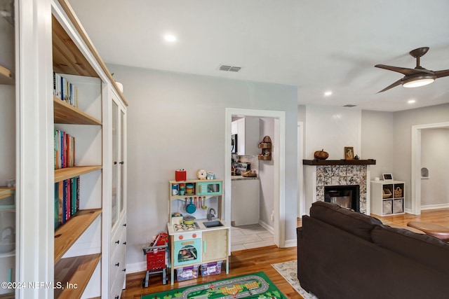 living room with a tile fireplace, ceiling fan, and light hardwood / wood-style floors