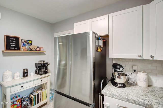 kitchen with tasteful backsplash, stainless steel refrigerator, light stone counters, and white cabinets