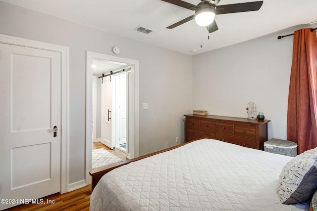 bedroom with ceiling fan, a barn door, wood-type flooring, and connected bathroom