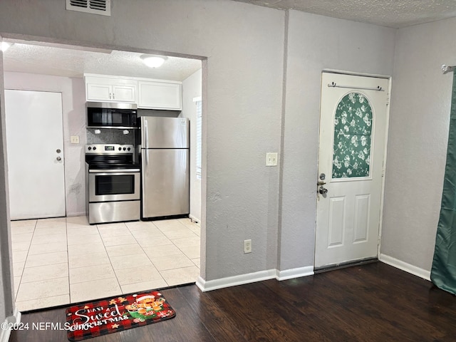 kitchen featuring white cabinets, a textured ceiling, stainless steel appliances, and light hardwood / wood-style flooring