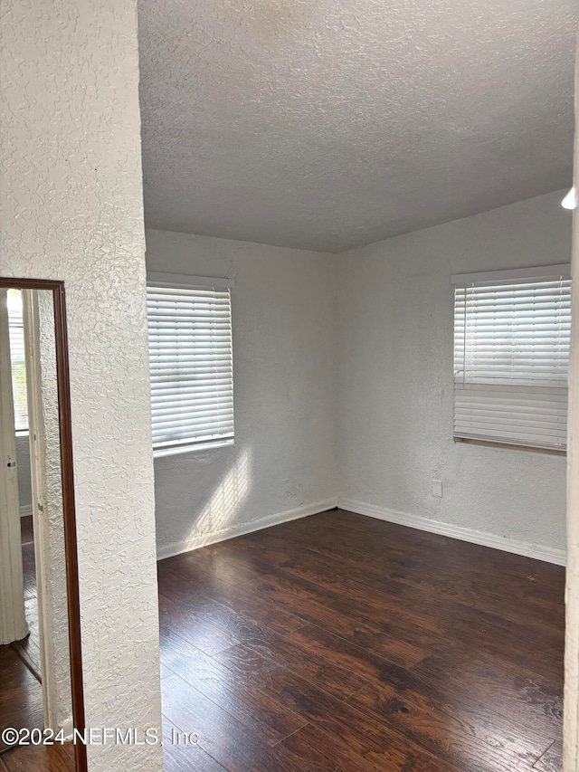 spare room featuring a textured ceiling, plenty of natural light, and dark wood-type flooring