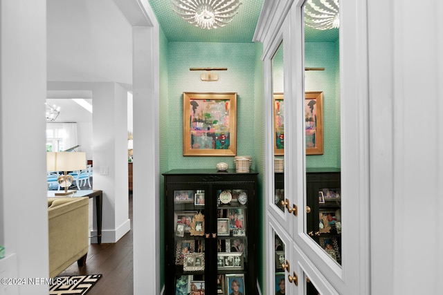 corridor with dark wood-type flooring and an inviting chandelier