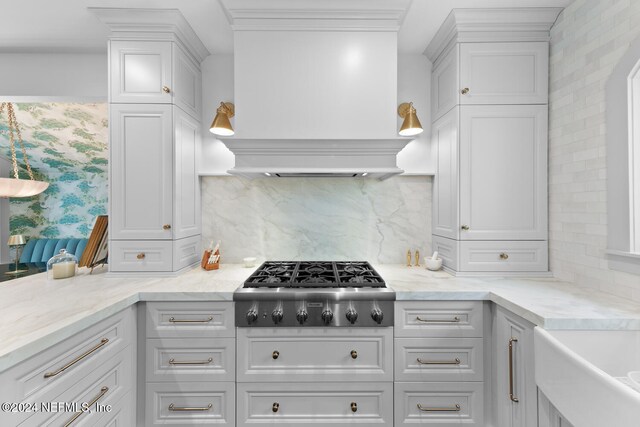 kitchen with white cabinetry, premium range hood, backsplash, stainless steel gas stovetop, and ornamental molding