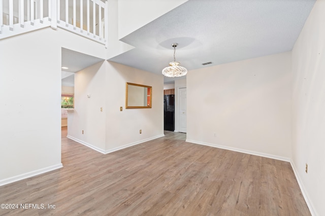 spare room with a textured ceiling, light wood-type flooring, and a notable chandelier