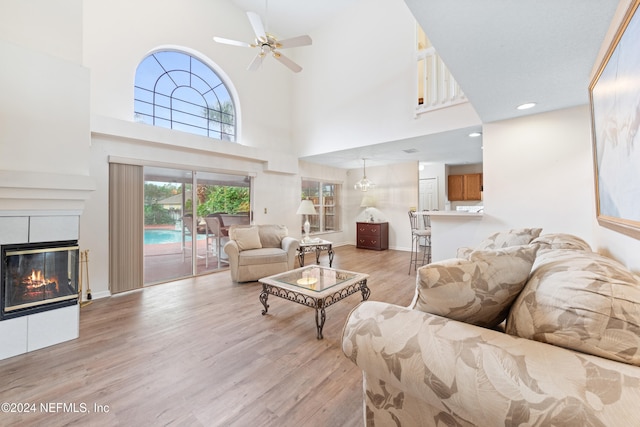 living room featuring a fireplace, light hardwood / wood-style flooring, ceiling fan, and a high ceiling