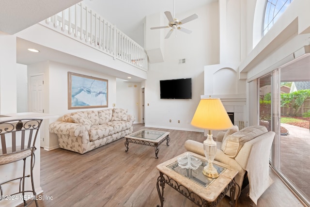 living room with a towering ceiling, light hardwood / wood-style flooring, ceiling fan, and a fireplace